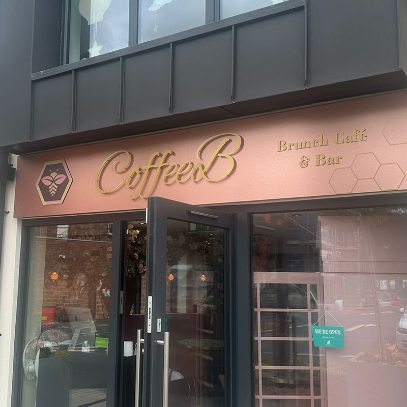 A rose gold sign hung above a retail shop door. The sign says CoffeeB Brunch Cafe & Bar