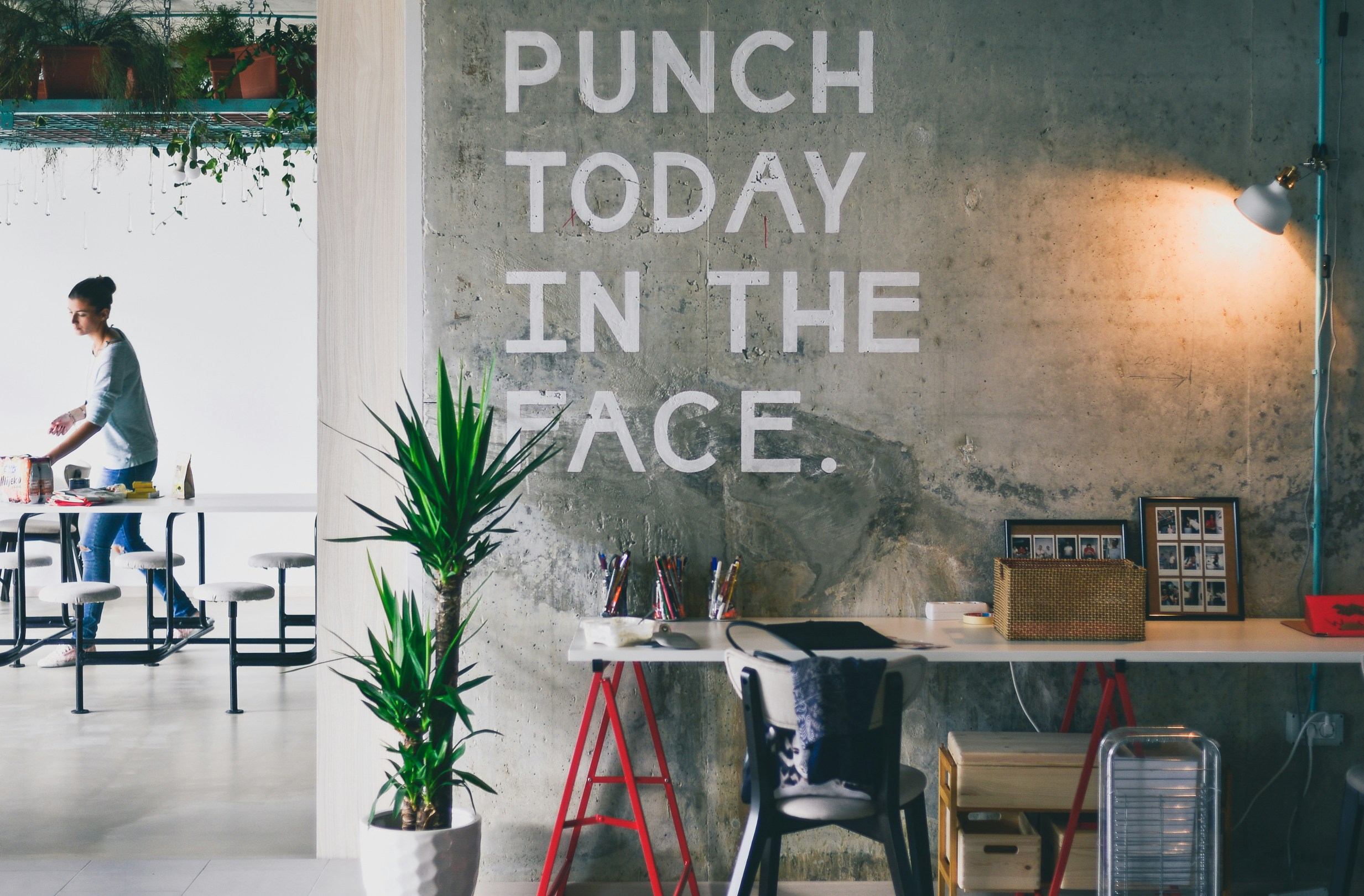 A sign spelling 'punch today in the face' on a wall above a desk in an office